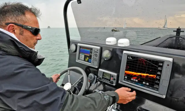 Un homme navigue, consultant un écran de sonar affichant des données sous-marines.