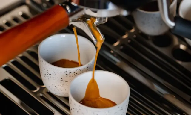 Frisch gebrühter Espresso fließt in zwei Tassen. Hoffentlich schmeckt er nicht zu sauer.