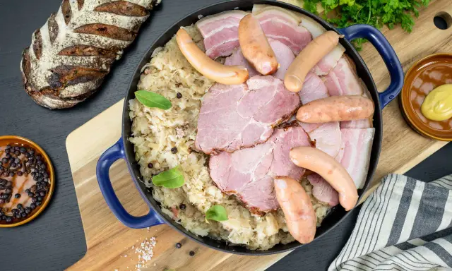 Un plat généreux de choucroute de Noël, garni de saucisses, jambon et lard, accompagné d'une miche de pain rustique.