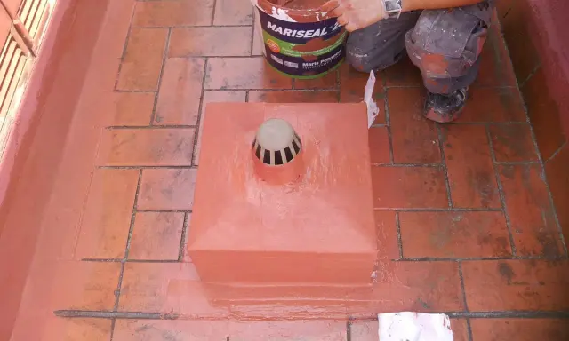 Persona aplica pintura para impermeabilizar terraza. Cubeta de Mariseal y desagüe en el centro.