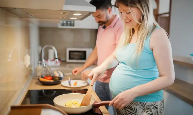 Schwangere Frau kocht Rührei, während ihr Mann daneben steht. Sie achtet auf ihre Ernährung, um Listeriose in der Schwangerschaft zu vermeiden.