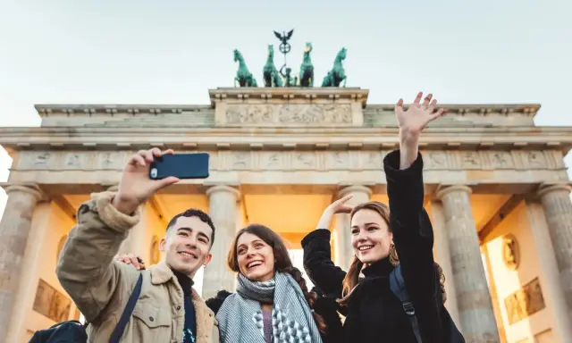 Tre glada vänner tar en selfie framför Brandenburger Tor, en ikonisk sevärdhet att se i Berlin.