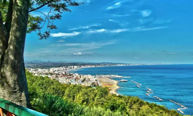 Vista panoramica della Riviera Romagnola con mare azzurro, spiagge affollate e una città costiera. Ideale per il turismo.