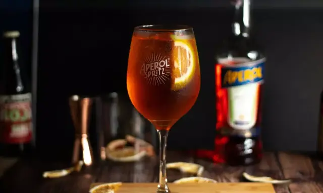 Orzeźwiający Aperol Spritz z plastrem pomarańczy, obok butelki Aperolu. Poznaj różne rodzaje Aperolu i jego zastosowania.