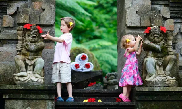 Bambini a Bali esplorano antiche statue decorate con fiori. Un'avventura indimenticabile per i più piccoli.