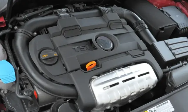 Silnik 1.4 TSI z widocznym logo VW. Czarna pokrywa silnika z napisem TSI i pomarańczową pętlą do sprawdzania oleju.