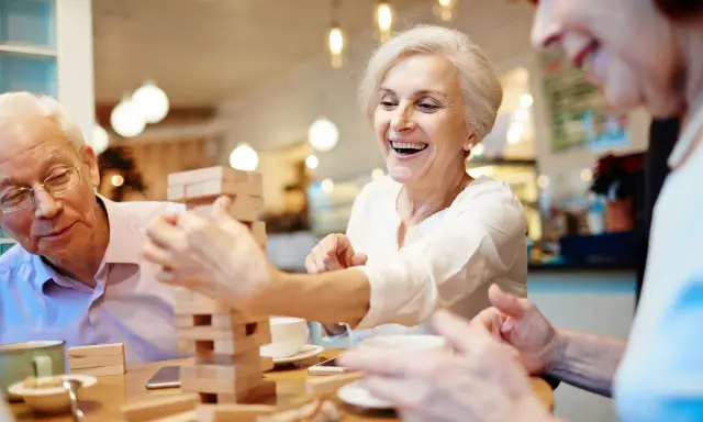 Anziani ridono giocando a Jenga, un esempio di iniziative per anziani che promuovono divertimento e socialità.