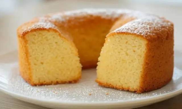 Un délicieux gâteau sans oeuf, saupoudré de sucre glace, est présenté sur une assiette blanche. Sa texture moelleuse est visible.
