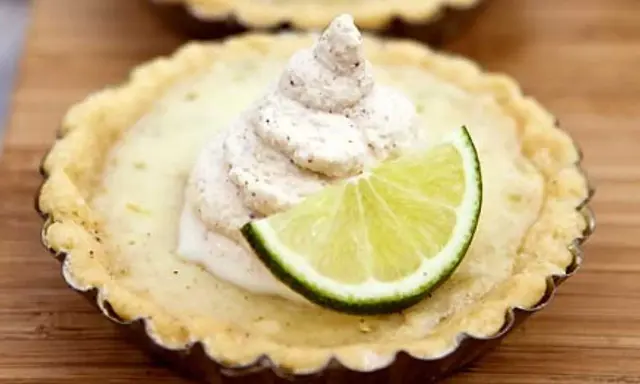En liten key lime pie med en virvel av gräddig topping och en limeklyfta.