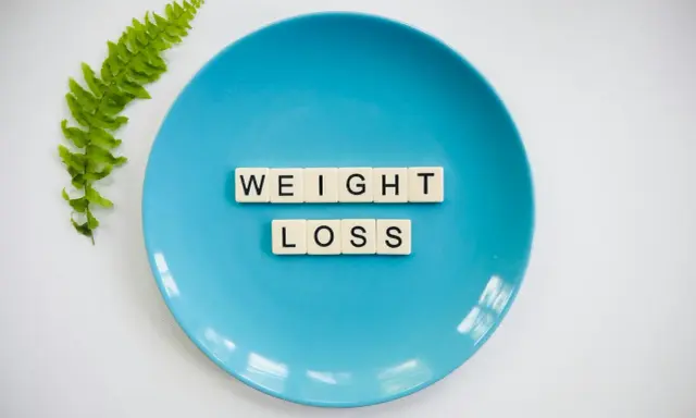 Niebieski talerz z literami tworzącymi napis "WEIGHT LOSS" i gałązką paproci. Pytanie o makro na redukcji?