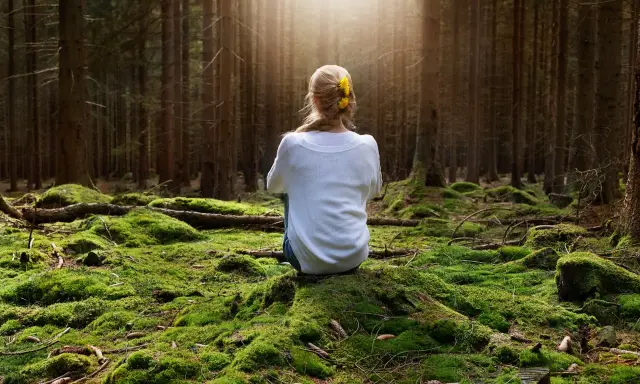 Frau sitzt im Wald auf moosbewachsenem Boden, sucht Ruhe, wenn sie immer gestresst und genervt ist.