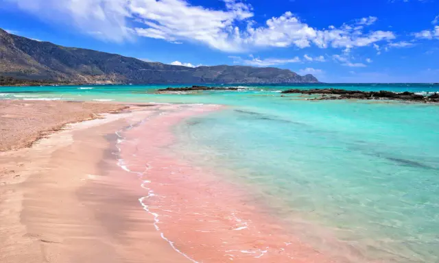 Różowa plaża Kreta kusi turkusową wodą i piaszczystym brzegiem. Góry w tle dodają uroku.