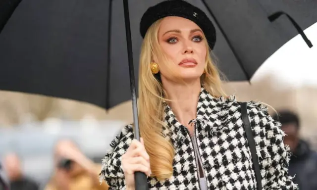 Mujer con boina negra y chaqueta a cuadros, sosteniendo un paraguas. Su maquillaje es un perfecto ejemplo de soft glam.