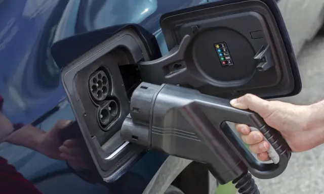 Mano insertando cargador en coche eléctrico. Averigua cuanto tarda en cargar un coche eléctrico en casa.
