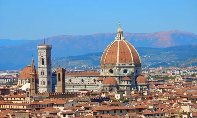 Vue panoramique de Florence avec le **dôme de Brunelleschi** dominant la ville, sous un ciel bleu clair.