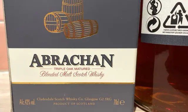 Elegancka butelka Abrachan Blended Malt Scotch Whisky, potrójnie dojrzewająca w dębie, z beczkami na etykiecie.