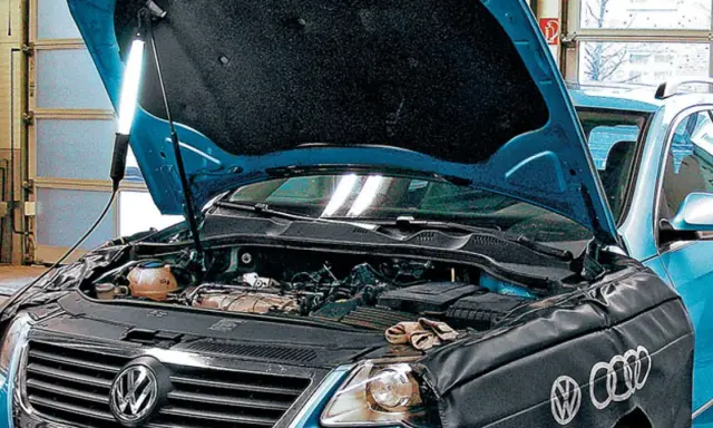 Pod maską niebieskiego VW z silnikiem 2.0 TDI, mechanik oświetla silnik lampą.