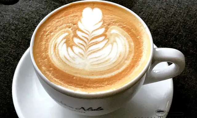Eine Tasse Cappuccino mit kunstvoller Barista Art, die ein Herz und Blätter zeigt.