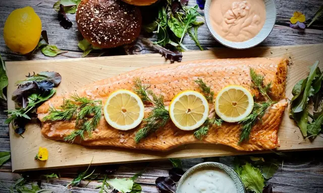 Flammlachs mit Zitronenscheiben und Dill, serviert mit cremigen Dips und frischem Salat als Beilagen.