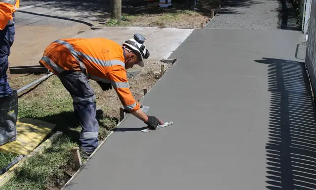 Robotnik wygładza świeży beton, zastanawiając się, ile kosztuje kubik betonu na nową ścieżkę.