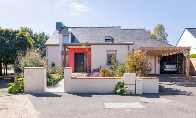 Maison moderne avec entrée rouge vif et carport en bois. Idéal pour estimer le prix rénovation maison m2.