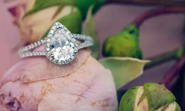 Un prezioso anello a goccia, simbolo di purezza e amore eterno, adagiato su un petalo di rosa.