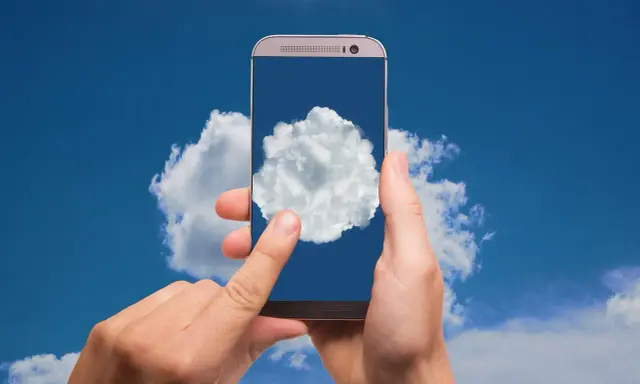 Dłonie trzymają telefon, na którego ekranie widać chmurę. To symbol tego, gdzie jest chmura w telefonie - w chmurze danych.