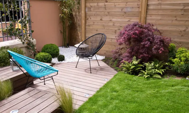Aménagement d'un petit jardin de 100m2 : terrasse en bois, mobilier design, gazon et végétation luxuriante pour un espace détente moderne.