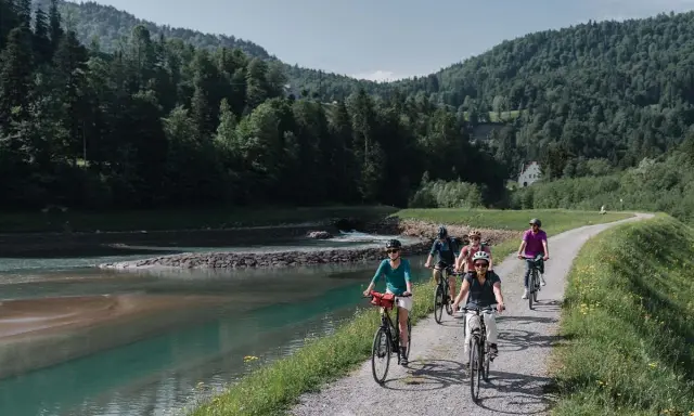 Gruppe genießt MTB Touren entlang eines Flusses mit bewaldeten Hügeln im Hintergrund.