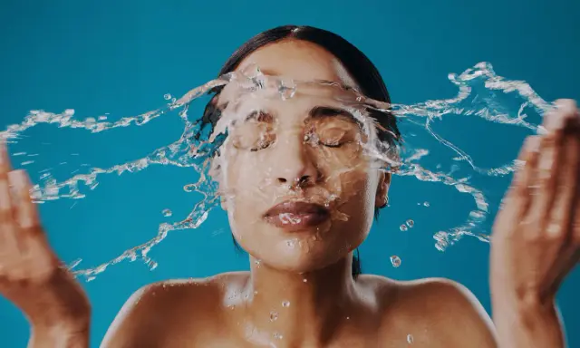Una mujer se lava la cara con agua fría, sintiendo el frescor en su piel.