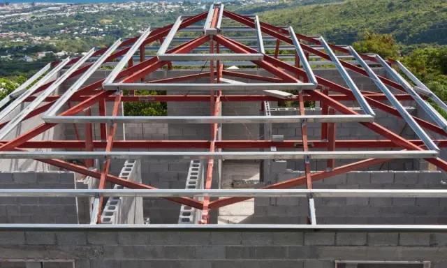 Structure métallique d'une maison en construction, avec des poutres rouges et grises. Un inconvénient potentiel de ce type de maison est la nécessité d'une isolation thermique soignée.