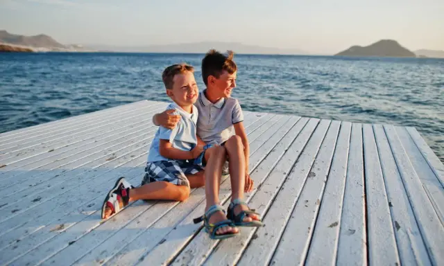 Dos niños sonríen sentados en un muelle blanco. ¡Ideas para que hacer en Murcia con niños!