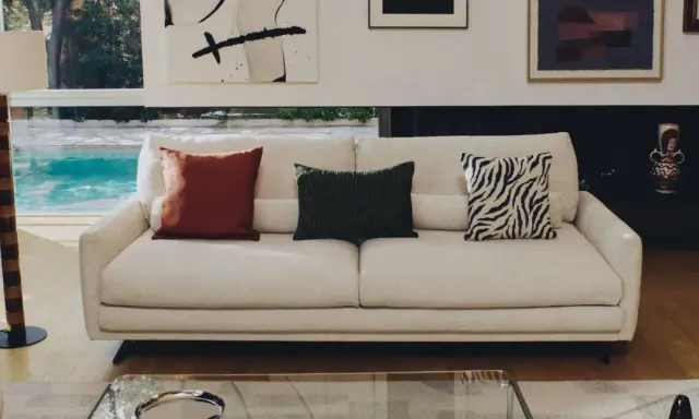 Sofá blanco con cojines decorativos: uno rojo, uno verde con textura y otro con estampado de cebra.