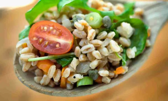 Un cucchiaio di farro condito con pomodorini, capperi e verdure fresche. Un'idea gustosa su come condire il farro per un pasto leggero e nutriente.