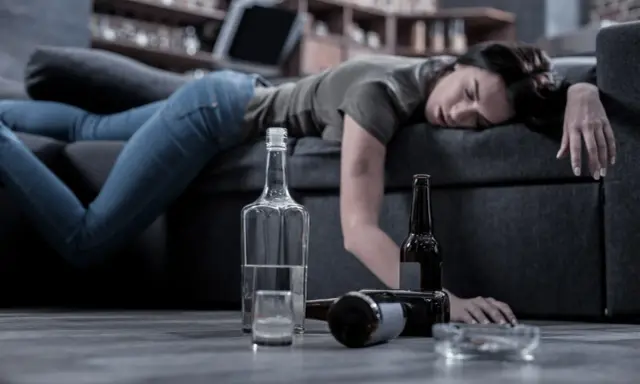 Kobieta leży nieprzytomna na kanapie, obok butelki i szklanka. Czy alkoholik może pić kontrolowanie? To pytanie pozostaje bez odpowiedzi.