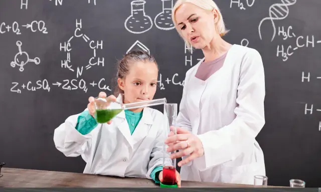 Nauczycielka chemii z pasją pokazuje uczennicy eksperyment. Ciekawe, ile zarabia nauczyciel chemii za taką pracę!