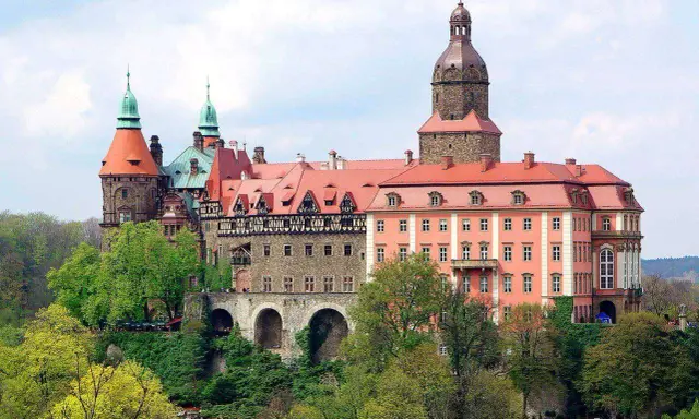 Malownicze zamki i pałace wokół Wrocławia, jak ten imponujący kompleks z wieżami i czerwonymi dachami, zachwycają architekturą i otoczeniem.