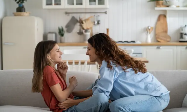 Madre e hija ríen en el sofá. Ella le enseña como es la primera regla de una niña: la empatía.