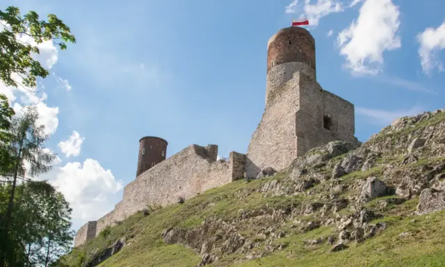 Ruiny zamku na skalistym wzgórzu w paśmie gór świętokrzyskich. Biało-czerwona flaga powiewa na wieży.