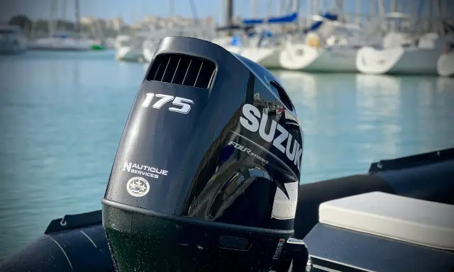 Moteur hors-bord Suzuki 175 CV, prêt pour une longue journée sur l'eau. Le mât de l'arbre est visible, avec des voiliers en arrière-plan.