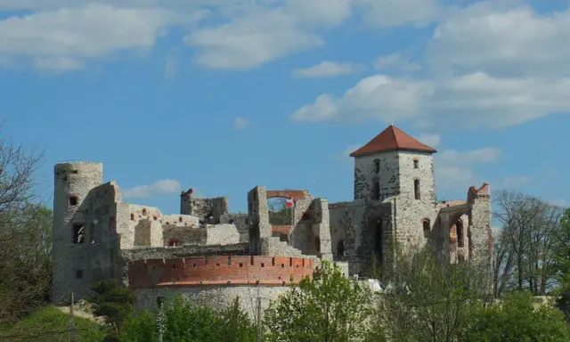 Zamek Tenczyn, ruiny kamiennej twierdzy z czerwoną cegłą i polską flagą, na tle błękitnego nieba z chmurami.