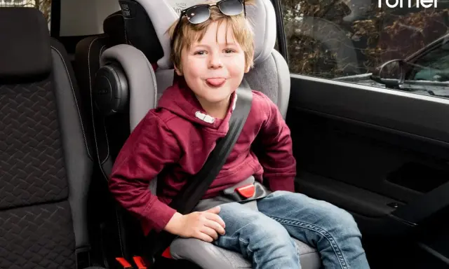 Chłopiec w foteliku samochodowym Britax Römer, zgodnym z normą ece r44/04, wyciąga język.