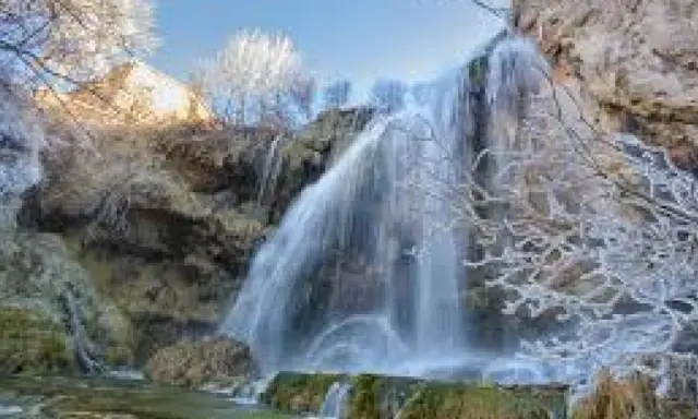 Cascada helada en el nacimiento del río Júcar, con ramas cubiertas de escarcha y agua cayendo sobre rocas.