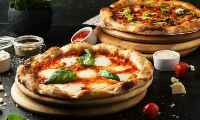 Dwie pyszne pizze, jedna margherita, druga z dodatkami. Obok sosy i pomidorki, idealne dodatki do pizzy.