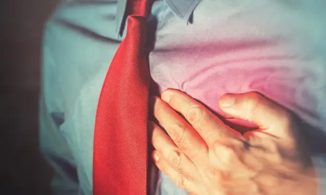 Mężczyzna w koszuli i krawacie trzyma się za klatkę piersiową, odczuwając ból. Może to być jeden z objawów niepożądanych diuretyków.