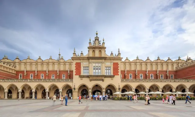 Sukiennice w Krakowie, zabytkowy budynek z arkadami, tętni życiem. Ludzie spacerują po Rynku Głównym, podziwiając architekturę.