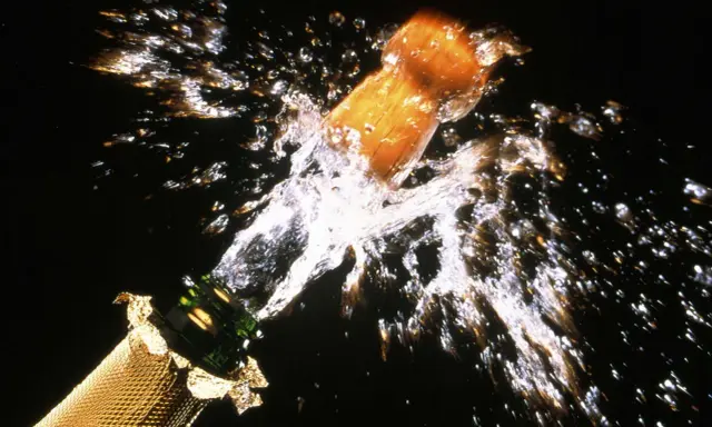 Le bouchon d'une bouteille de champagne s'envole dans un jet d'eau et de bulles, un moment de joie pour sabler le champagne.