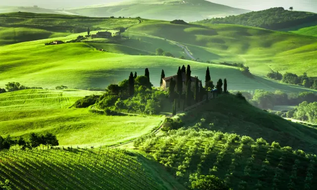 Colline verdi ondulate in Toscana, con una villa su una collina circondata da cipressi. Un sogno per un viaggio in Toscana.