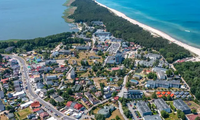 Dąbki atrakcje: widok z lotu ptaka na nadmorską miejscowość z plażą, lasem, jeziorem i zabudowaniami.