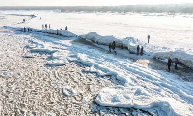 Ludzie spacerują po zamarzniętej plaży z lodowymi formacjami przypominającymi góry.